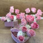 Нежна подаръчна кутия във формата на сърце с розови рози, бели хризантеми, парфюм и празничен медальон „Честит празник“.