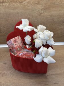 Романтична подаръчна кутия във формата на сърце с бели рози, шоколад Gucci Flora и празничен медальон „Честит празник“.
