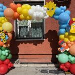 Празнична арка от балони с тематична училищна декорация, пчеличка, слънце, звънец и молив, подходяща за откриване на учебната година и първия учебен ден.