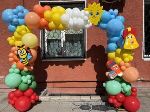 Празнична арка от балони с тематична училищна декорация, пчеличка, слънце, звънец и молив, подходяща за откриване на учебната година и първия учебен ден.